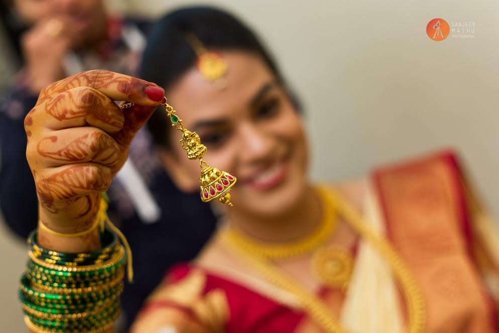 bride holds up her jhumka and smiles